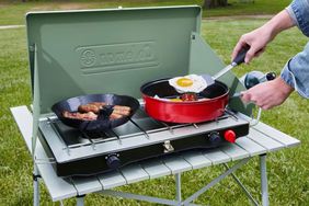 A person cooking on a Coleman Cascade Classic Camp Stove outside