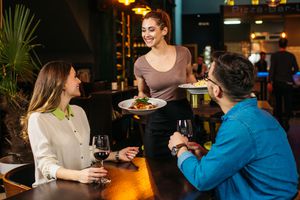 female server at restaurant brings dishes to two diners