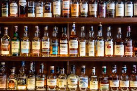 A huge selection of different malt Scotch whisky bottles in a row and displayed on wooden shelves at a bar in London, UK.