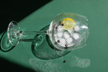 A glass of gin and ice on a green background.