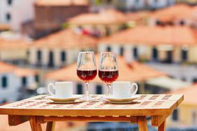 Two glasses of Madeira wine and two cups of fresh espresso coffee on a table with a view to Funchal town, Madeira, Portugal